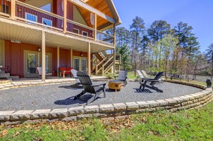 A two-story wooden cabin with a covered porch, outdoor seating area with Adirondack chairs, and a stone fire pit.