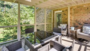 Un patio techado al aire libre con mobiliario de mimbre, una mesa de vidrio y una pared de ladrillo.