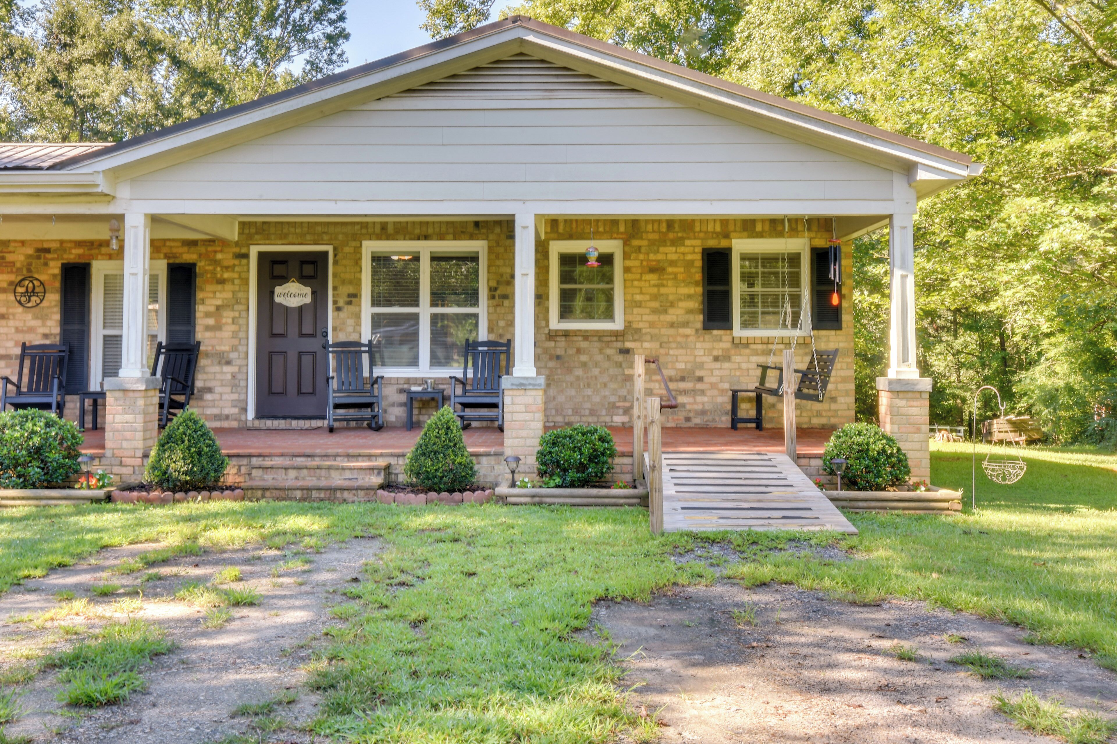 A two-story house with a front porch, a door with a 'Welcome' sign, and a small front yard with a lawn and a gravel path.