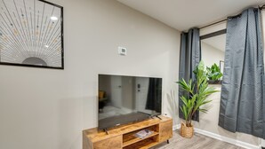 Un salon moderne avec un téléviseur à écran plat posé sur un meuble télé en bois, un grand miroir au mur et une plante en pot.