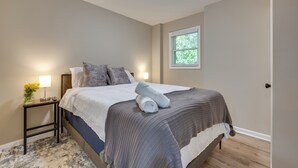 Un lit bien fait, avec une couverture à rayures, une lampe de chevet et une fenêtre donnant sur un paysage verdoyant.