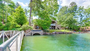 A wooden bridge over a green body of water, leading to a building with a stone facade and a balcony. - Waterfront Escape on Blue Ridge Lake w/ Dock! (Morganton)