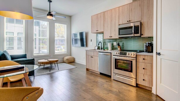 A modern kitchen with wooden cabinets, stainless steel appliances, and a dining area with a glass table and chairs. - Modern Atlanta Townhome Rental ~ 2 Mi to Downtown! (Atlanta)