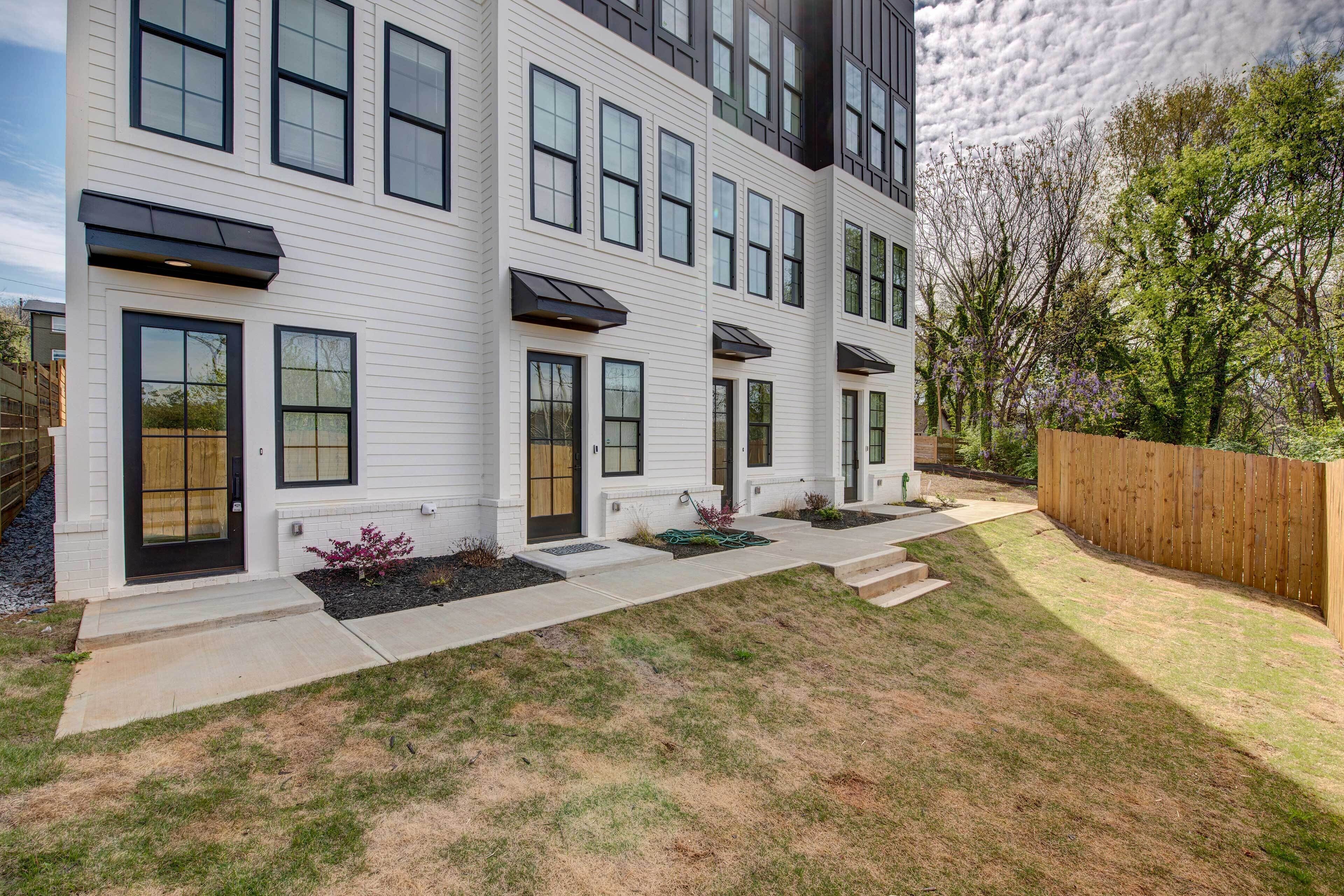 A modern two-story house with a front yard, a wooden fence, and a garden area.
