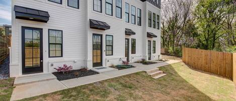A modern two-story house with a front yard, a wooden fence, and a garden area.