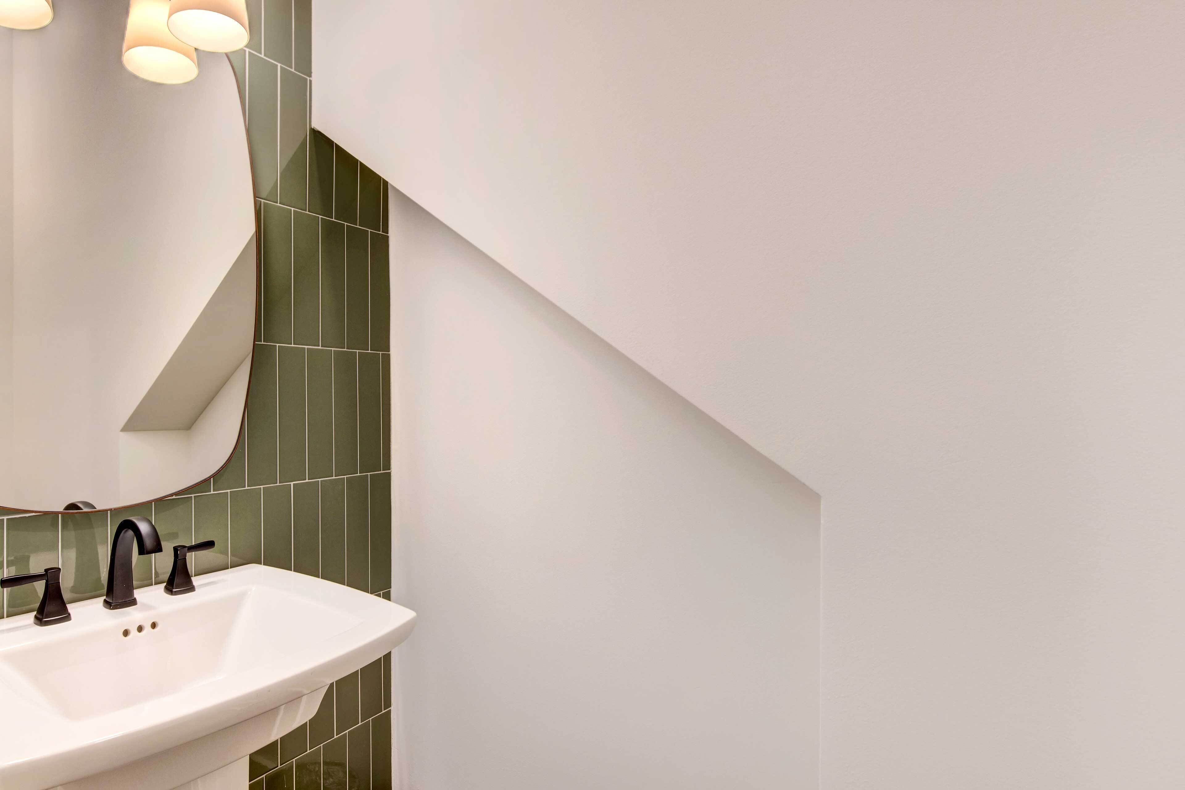 A modern bathroom with a white sink, dark faucet, and green tiles.