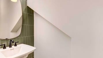 A modern bathroom with a white sink, dark faucet, and green tiles.