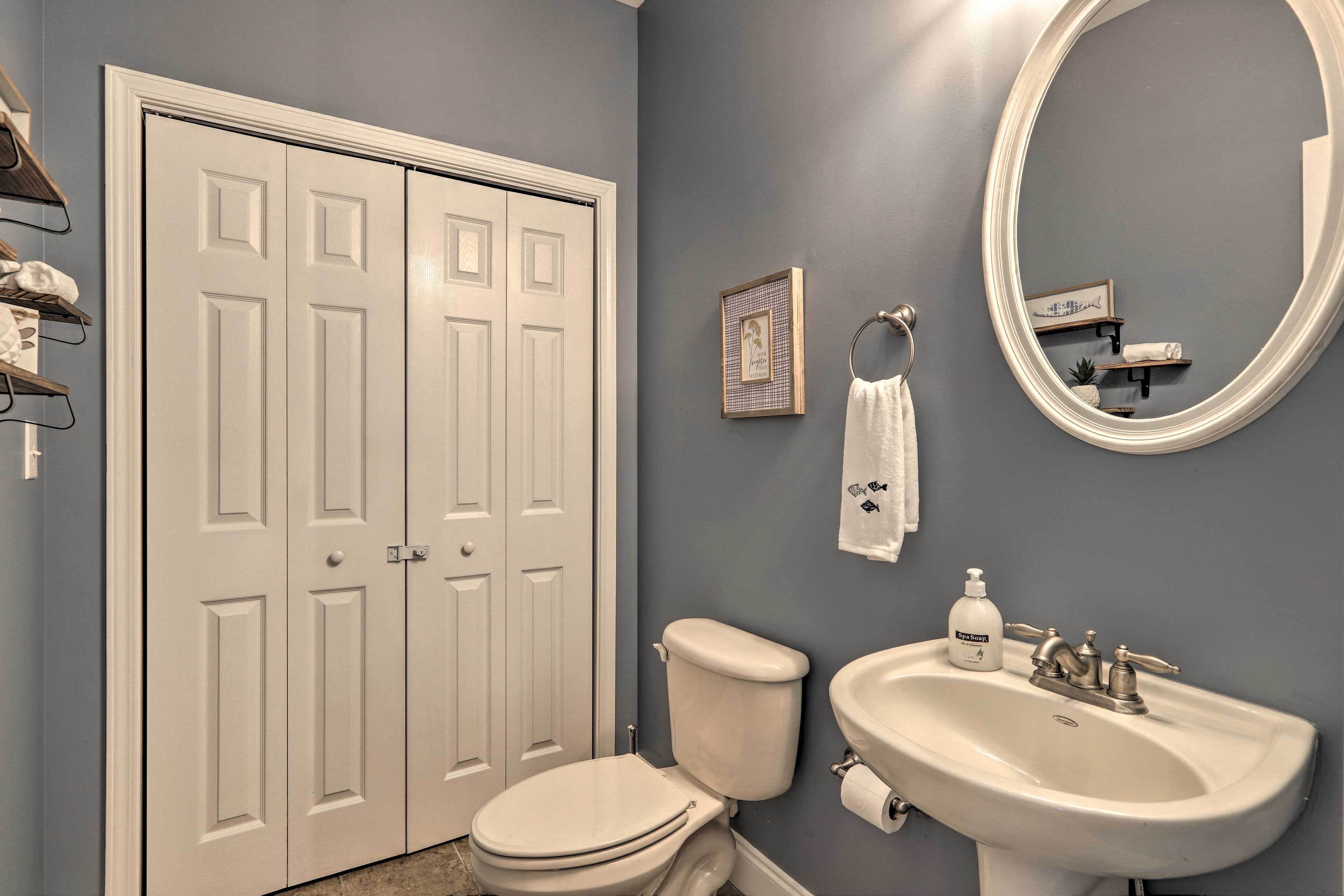 A bathroom with a toilet, sink, and a large mirror. There are towels hanging on the wall and a framed picture above the mirror.