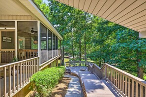 A covered outdoor deck with a wooden railing, a "Welcome" sign, and a view of a forested area.