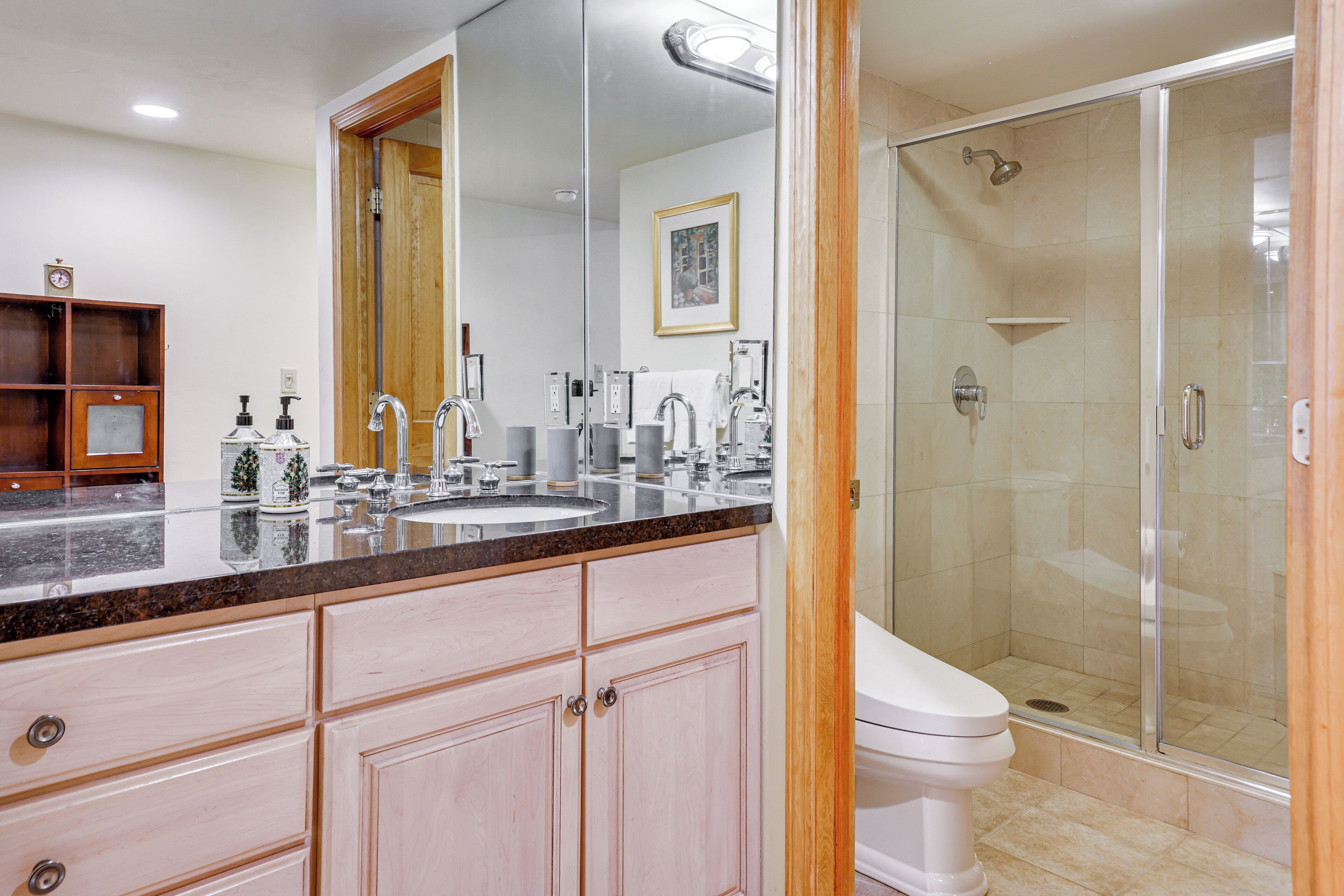 A bathroom with a large mirror, a sink, a toilet, and a glass-enclosed shower.