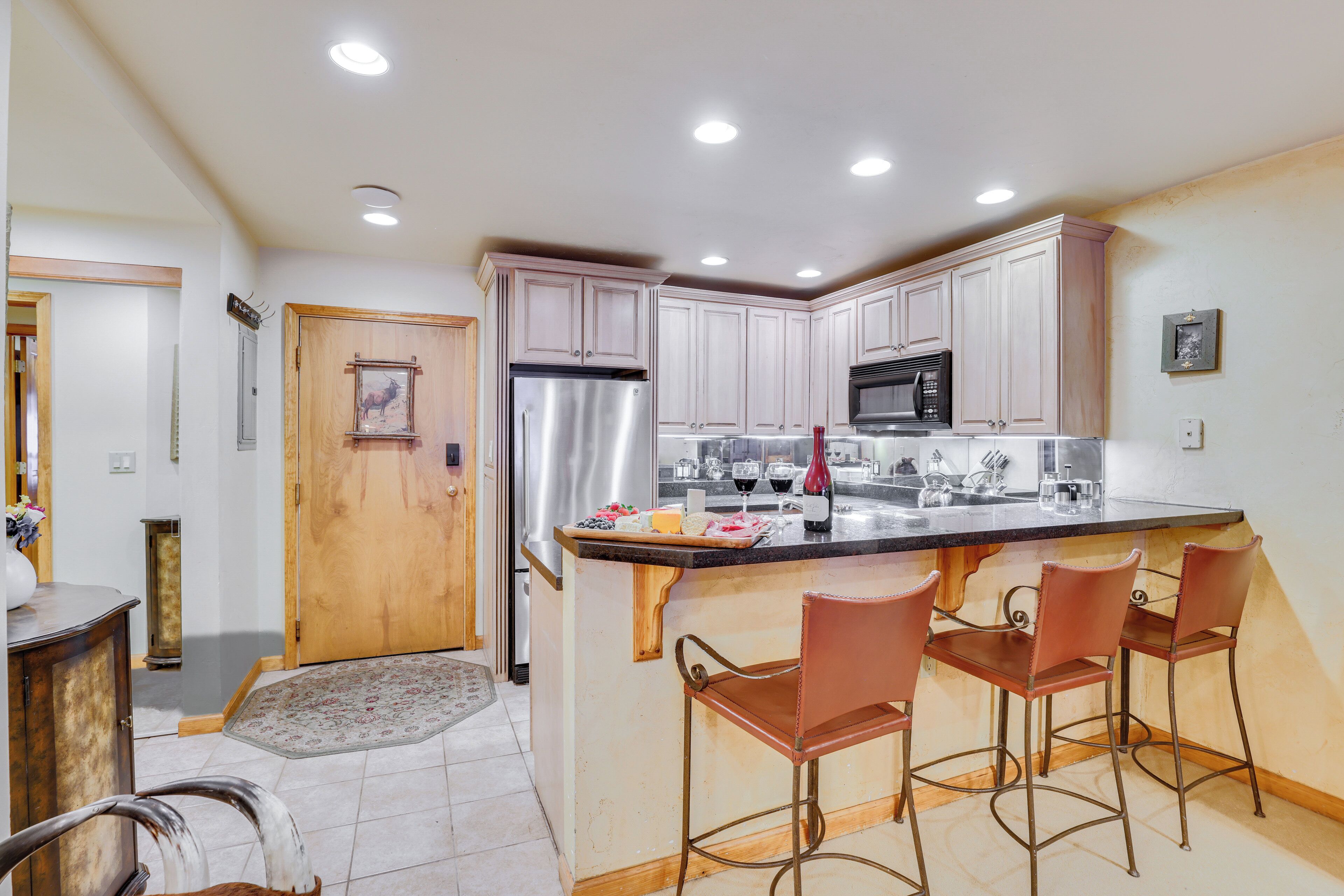 A kitchen with white cabinets, stainless steel appliances, and a bar area with four stools.