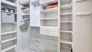 Um closet espaçoso com várias prateleiras, gavetas e espaço para pendurar roupas, apresentando uma organização impecável.