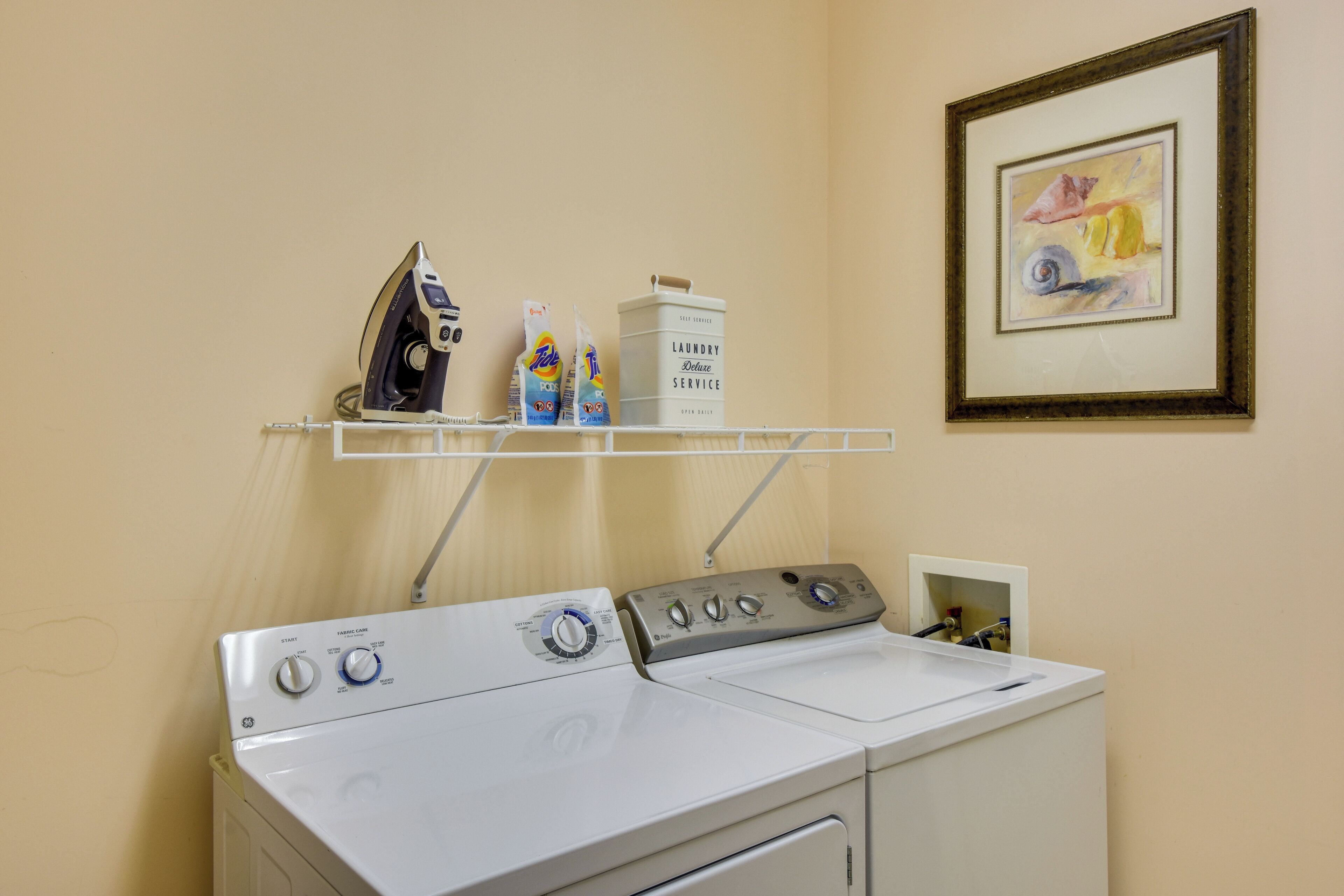 A laundry area with a washing machine, an iron, and detergent bottles on a shelf.