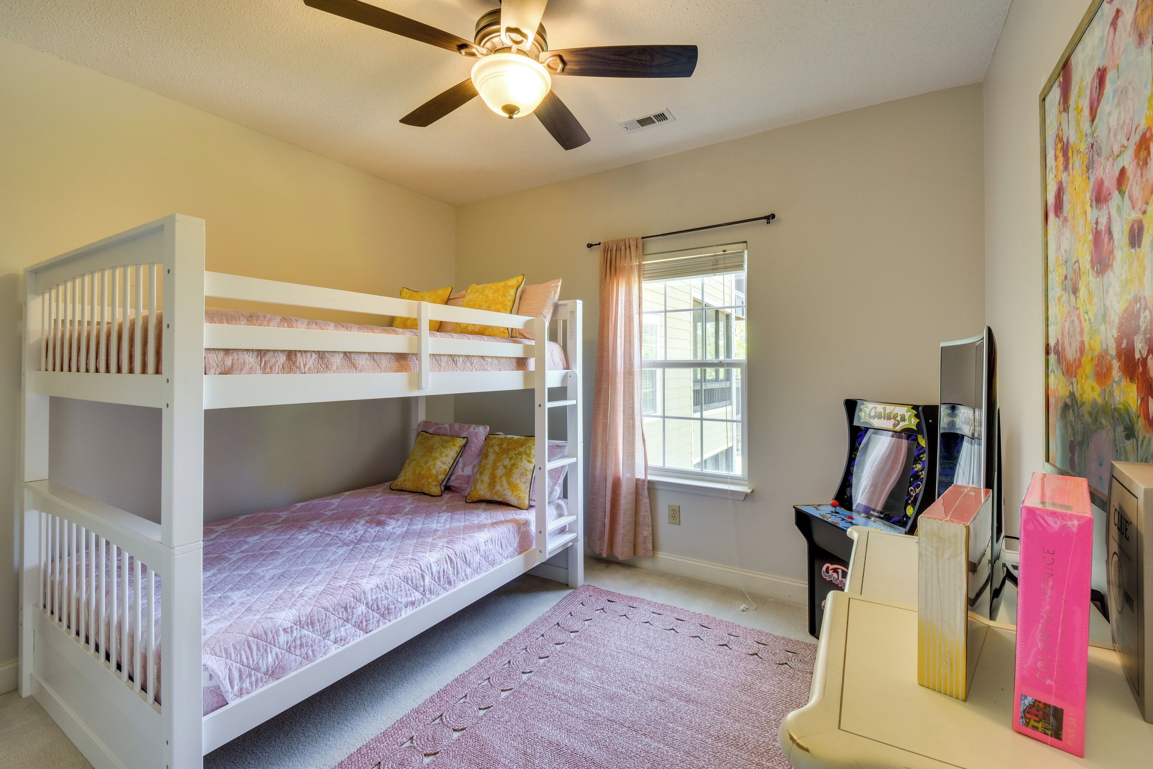 A bunk bed room with a ceiling fan, a window with curtains, and a gaming console.