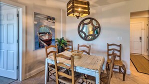 A dining area with a wooden table, chairs, a hanging light fixture, a wall-mounted mirror, and a framed picture. - 3rd-floor Riverfront Condo: Walk to Downtown Eats! (Darien)