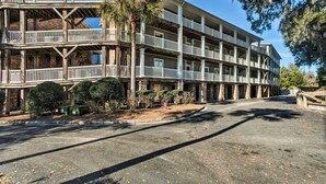 A multi-story building with balconies, a parking area, and a small garden with bushes and a palm tree. - 3rd-floor Riverfront Condo: Walk to Downtown Eats! (Darien)