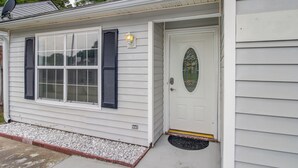 A single-story house with a white exterior, a front door with a decorative glass panel, and a small porch area with a doormat.