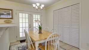 A dining area with a wooden table and white chairs, a chandelier, and a door with frosted glass panels.