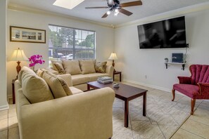 A living room with beige sofas, a coffee table, a red armchair, a TV, and a ceiling fan. - Savannah Vacation Rental ~ 8 Mi to River Street! (Savannah)