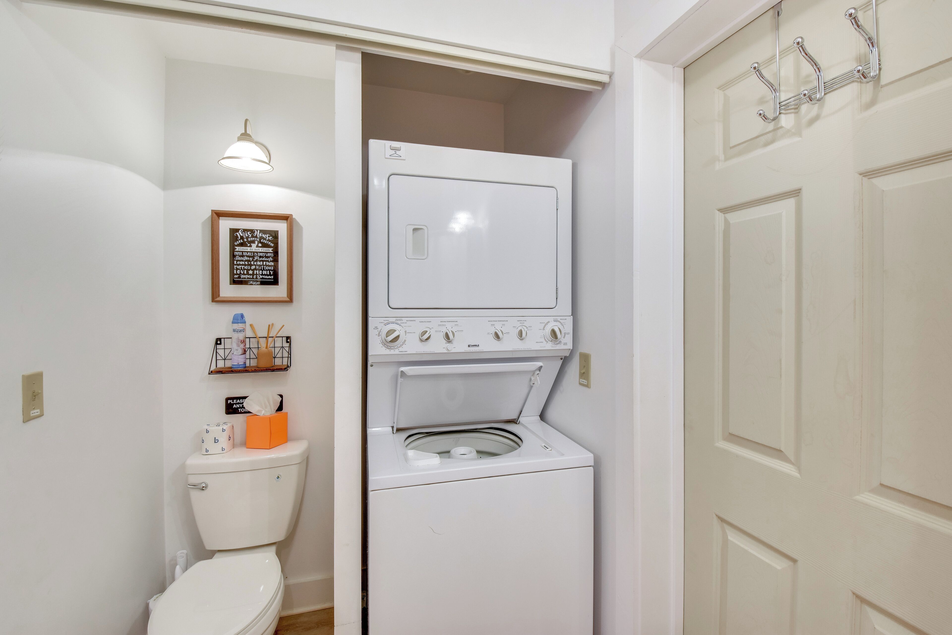 Une petite buanderie équipée d’un lave-linge et d’un sèche-linge à chargement frontal, de toilettes et d’une étagère où sont rangés les articles de toilette.