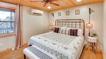 A bedroom with a wooden ceiling, a bed with floral bedding, a bedside table with a lamp, and a window with curtains.