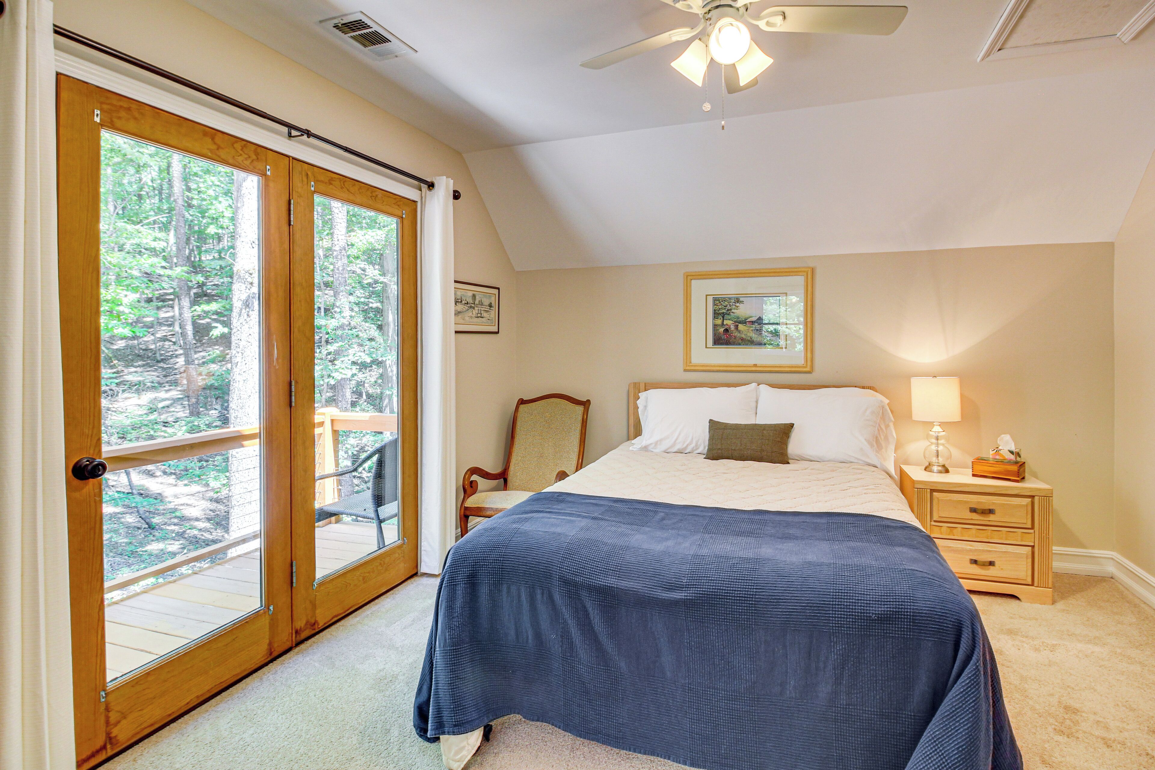 A bedroom with a large bed, a nightstand, a chair, and a window with a view of trees.