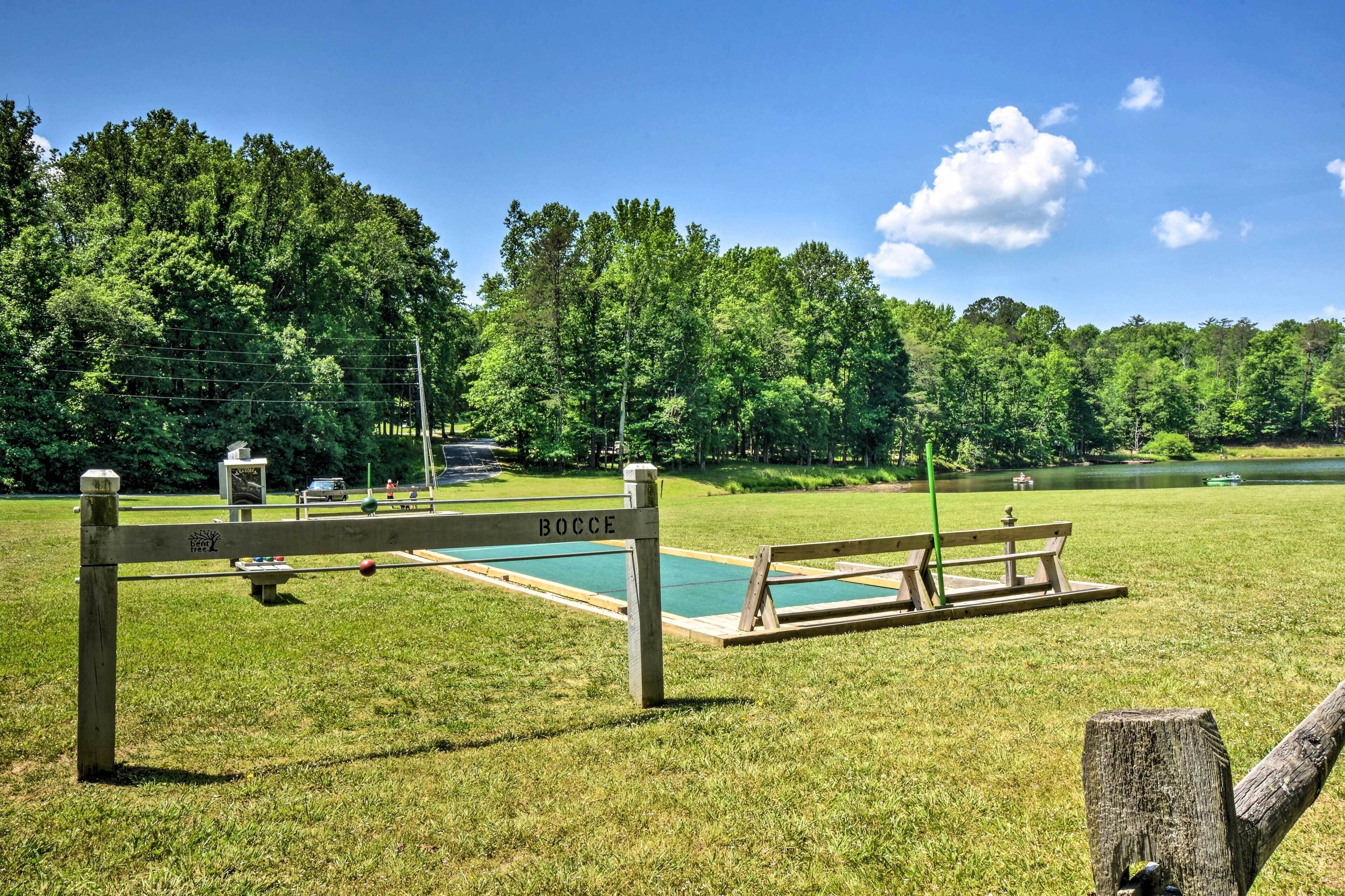 A bocce court with a wooden fence labeled "BOCCE," surrounded by a grassy field and trees.