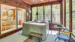 A wooden cabin interior with a hot tub, a dining area with a table and chairs, and large windows offering a view of the forest. - North Georgia Cabin w/ Hot Tub & Community Perks! (Jasper)