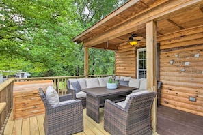 A wooden deck with wicker furniture and a table, surrounded by trees.