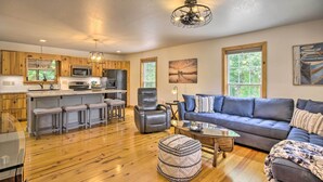 A spacious living area with a wooden floor, a blue sofa, a leather chair, and a kitchen area with wooden cabinets and a microwave.
