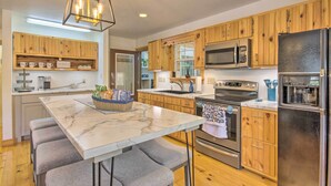 A modern kitchen with wooden cabinets, a marble island, and stainless steel appliances.