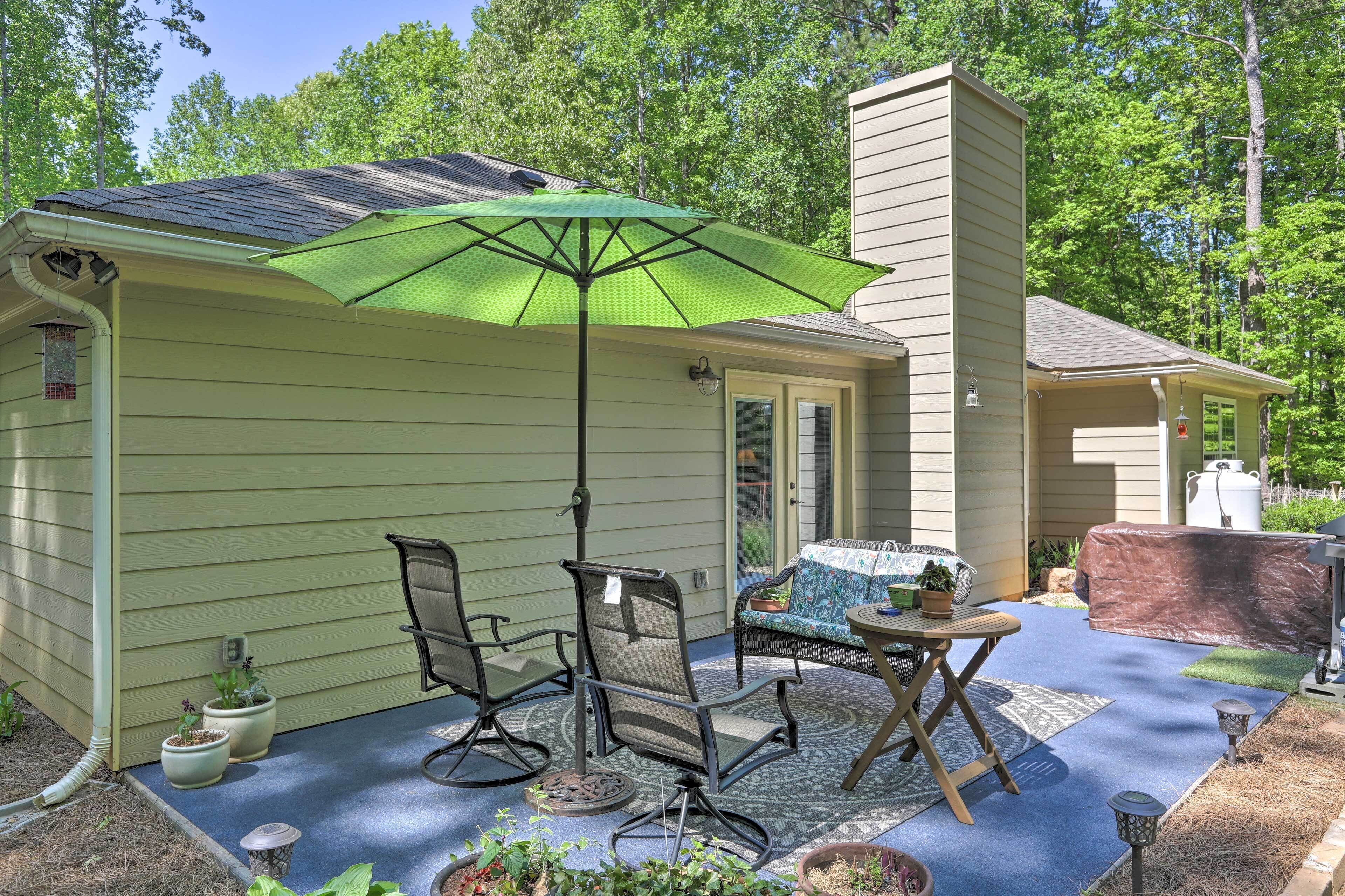 Une terrasse couverte avec une table et des chaises, un parasol vert et des plantes en pot.