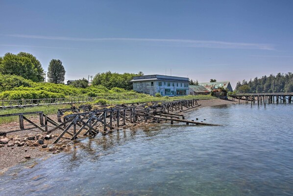 A riverside building with a dock extending into the water, surrounded by greenery and trees. - Waterfront Apt w/ Mtn View, Walk Into Town! (Craig)