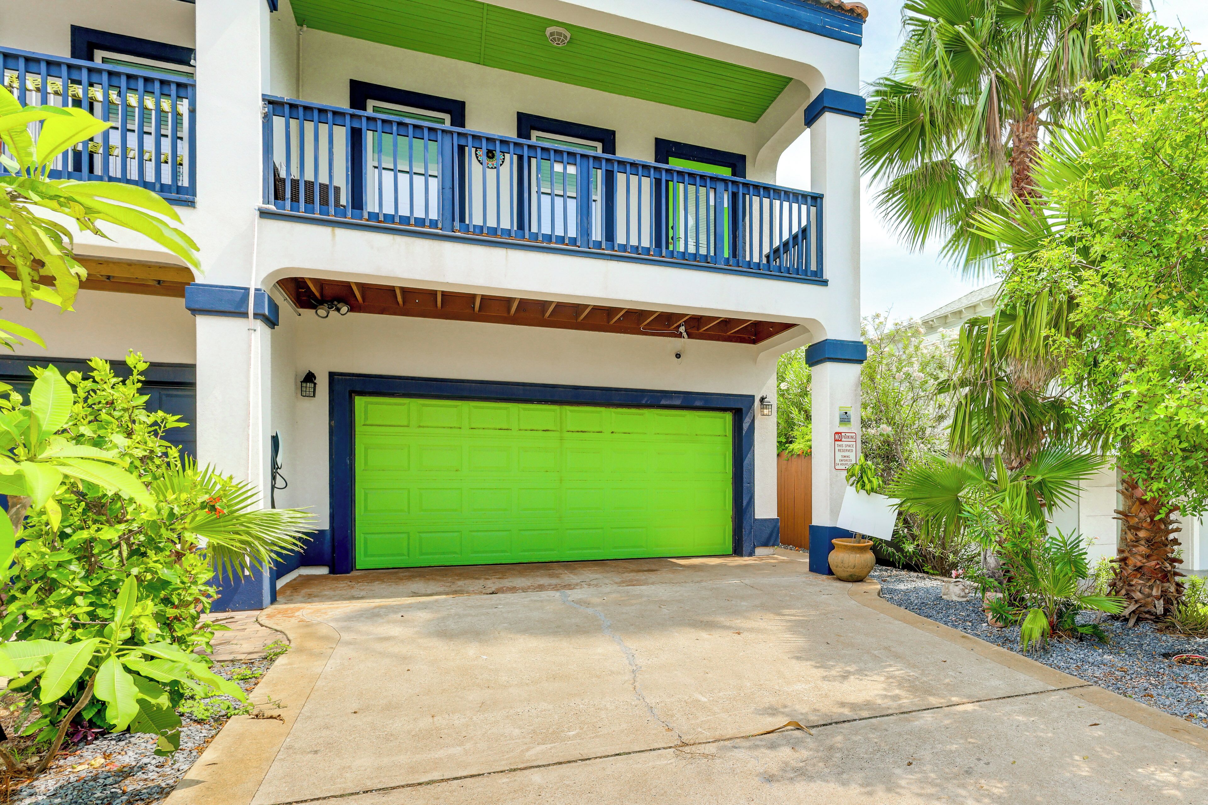 A two-story building with a green garage door, blue railings, and a balcony.