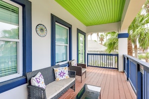 A covered porch with a sofa and chairs, a decorative plate on the wall, and a view of palm trees. - Steps to Beach: Oceanside Townhome w/ Heated Pool (South Padre Island)