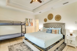 A bedroom with a bunk bed, a large bed with a headboard, and a bedside table with a lamp. - Steps to Beach: Oceanside Townhome w/ Heated Pool (South Padre Island)
