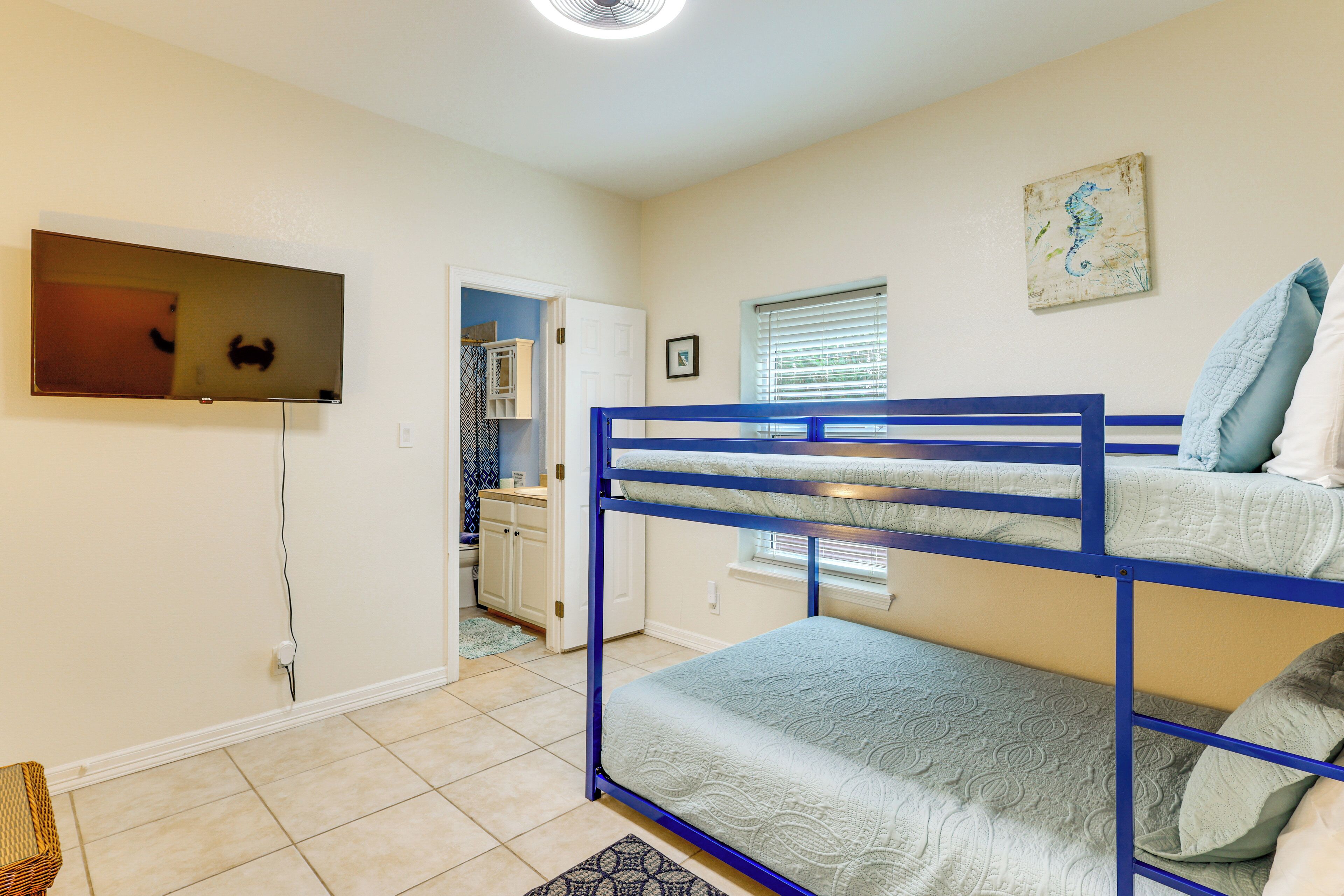 A bunk bed room with a television, a window with blinds, and a door leading to a bathroom.