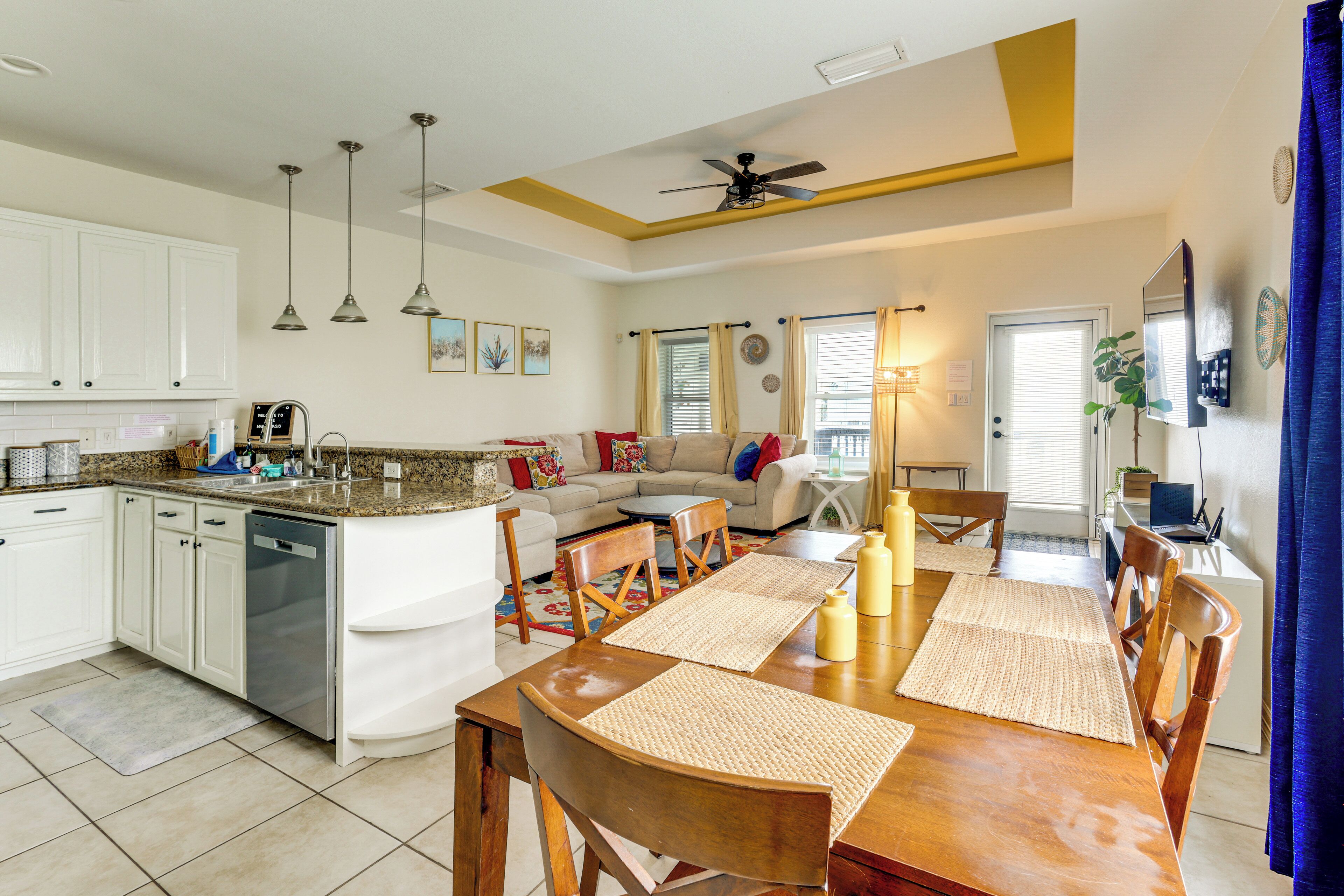 A modern kitchen with white cabinets, a dining area with a wooden table and chairs, and a ceiling fan.
