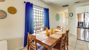 Un comedor con mesa de madera, sillas y cortinas azules.