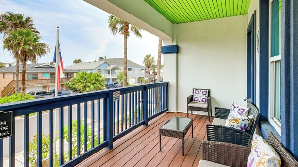 A balcony with a green ceiling, wicker furniture, and a view of palm trees and buildings.