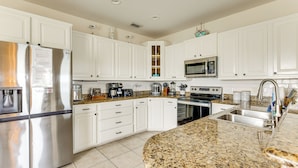 A modern kitchen with white cabinets, stainless steel appliances, granite countertops, and a built-in microwave.