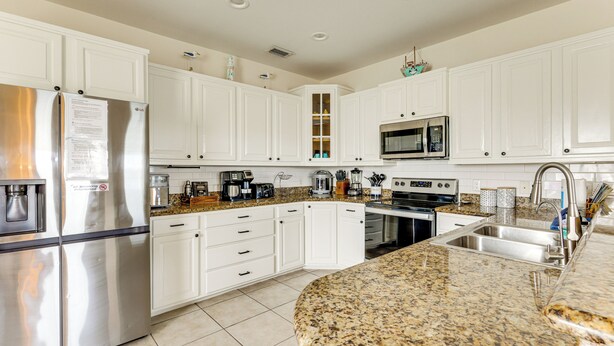 Una cocina moderna con gabinetes blancos, electrodomésticos de acero inoxidable, encimeras de granito y microondas integrado.