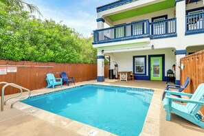 A swimming pool with lounge chairs, a wooden fence, and a building with balconies. - Steps to Beach: Oceanside Townhome w/ Heated Pool (South Padre Island)