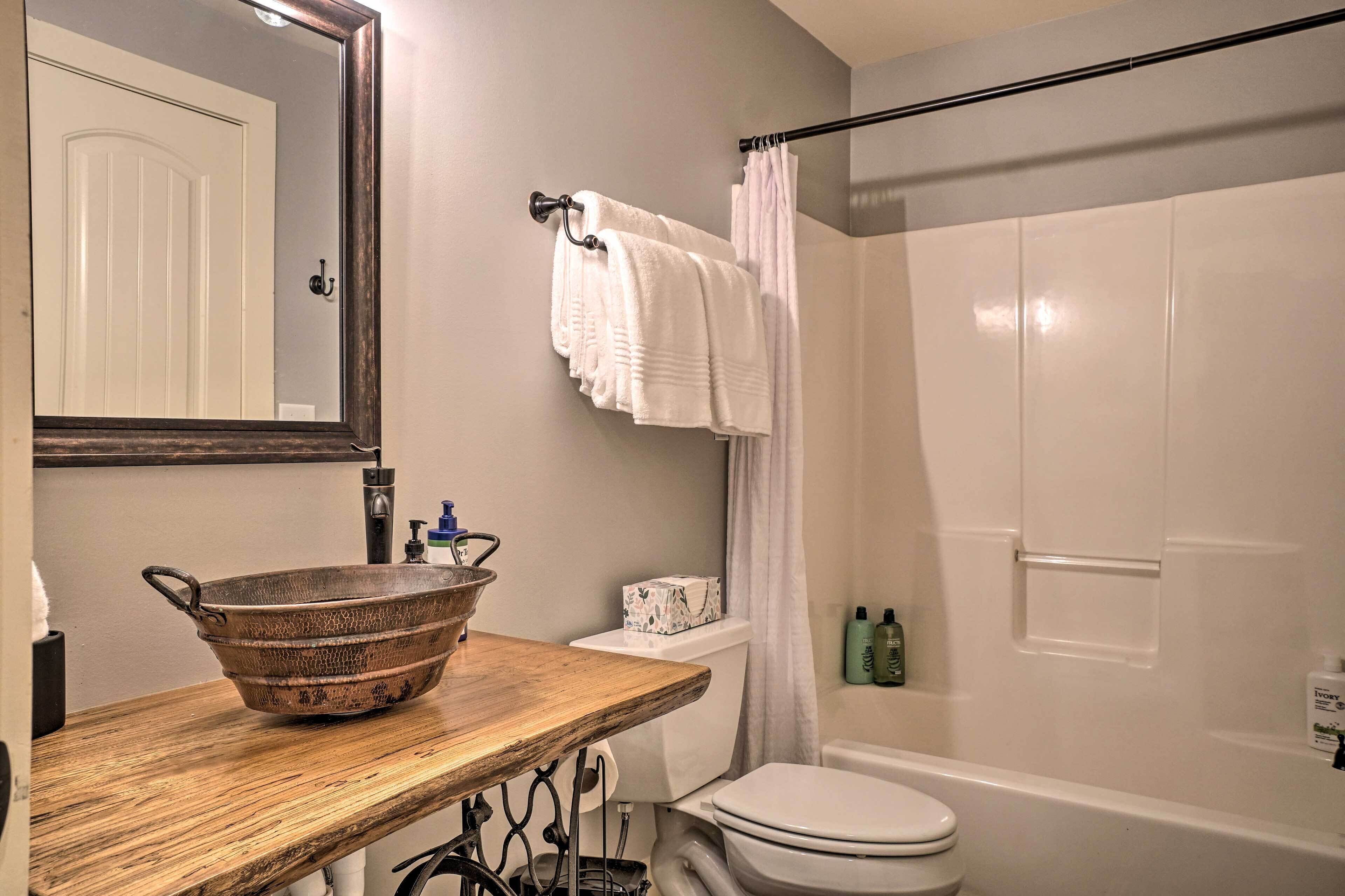Une salle de bain avec un meuble-lavabo en bois, un grand miroir, des toilettes blanches, un rideau de douche et une baignoire.