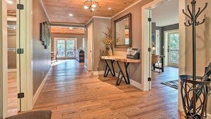 A spacious hallway with wooden flooring, a central table with a vase, and a coat rack. - Riverfront Tallulah Falls Cabin w/ Hot Tub! (Lakemont)