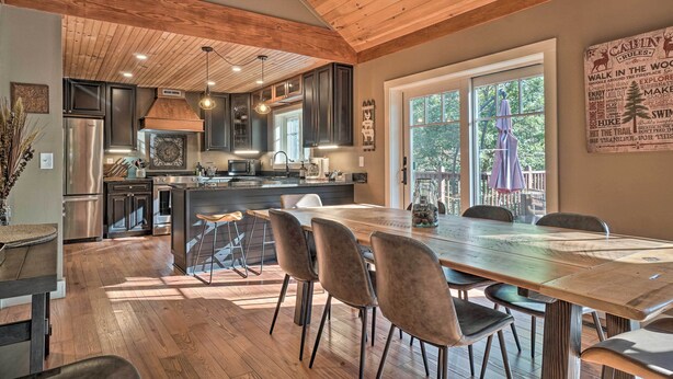 A spacious kitchen with dark cabinets, a large island, and a dining area with a wooden table and chairs. - Riverfront Tallulah Falls Cabin w/ Hot Tub! (Lakemont)