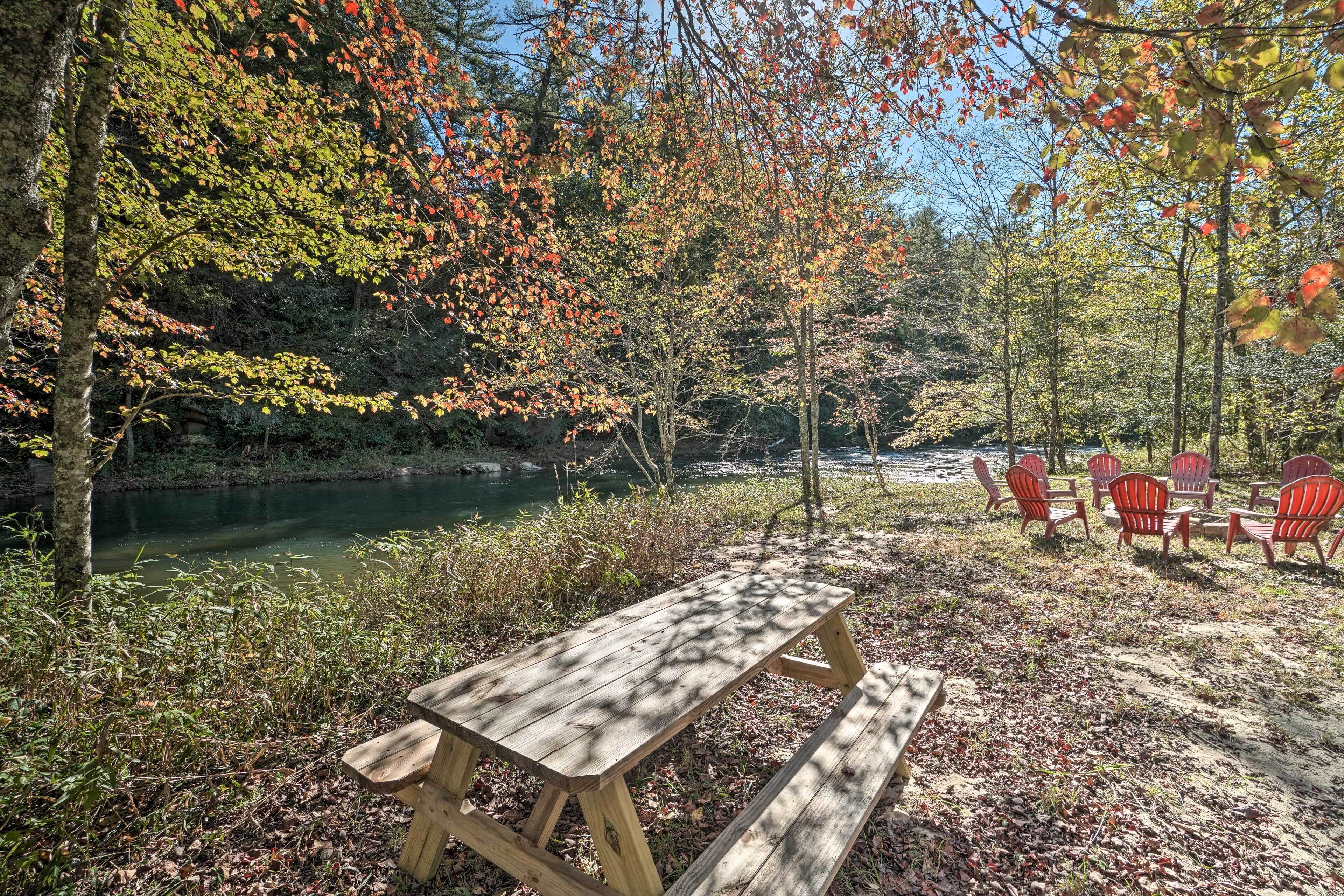 Una mesa de picnic y sillas rojas junto a un río en un bosque.