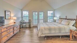 Une chambre à coucher avec un grand lit, une commode en bois, un bureau et une chaise, offrant une vue sur l’extérieur par les fenêtres.