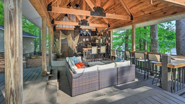 Un espace extérieur aménagé, abrité et doté de canapés et de tables, entouré de poutres en bois et offrant une vue sur les arbres.