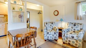 A dining area with a wooden table and chairs, two patterned armchairs, a clock, and a window with curtains. - Budget-friendly Tucson Studio: 2 Mi to University! (Tucson)